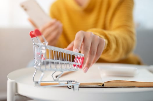 A close-up of a woman touching a mini shopping cart model on a table. shopping online, lifestyles photo