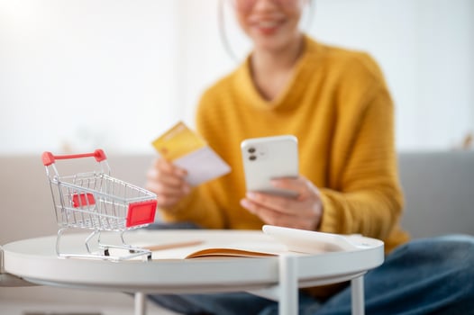 A mini shopping cart or trolley on a round table, with a blurred view of a woman sitting on a couch. photo
