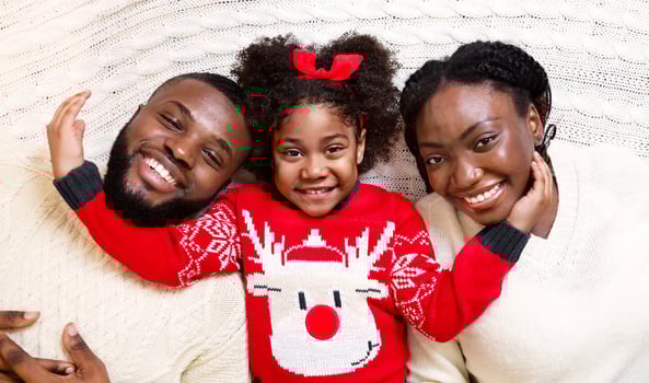 Christmas family. Happy afro mom,dad and daughter lying together on white knitted blanket photo