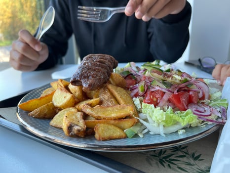 Unrecognized man holding plastic fork. With served Kebab with French fries and salad on a plate on white table in a restaurant photo
