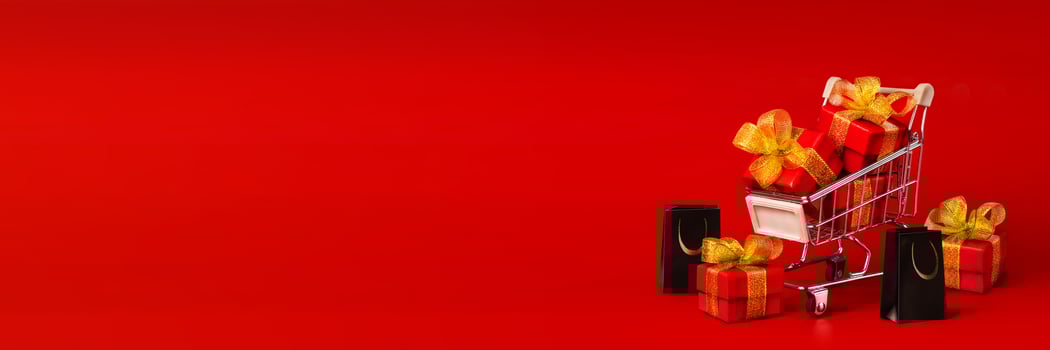A shopping cart with red gifts with gold bows and black shopping bags on a red background. Holidays, gifts, shopping copy space long horizontal banner photo