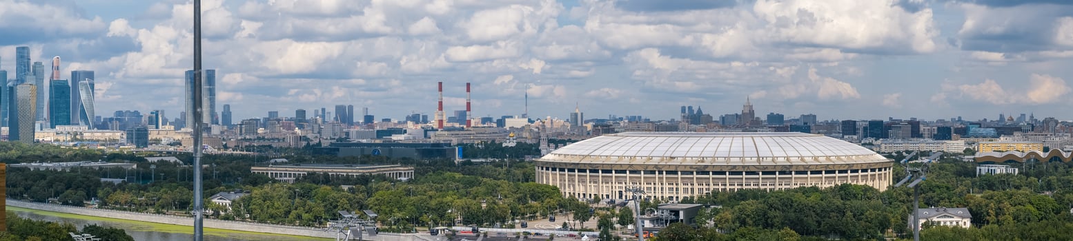 The iconic Luzhniki Stadium is nestled within Luzhniki Park, with the modern Moscow City skyline rising in the background under blue skies photo