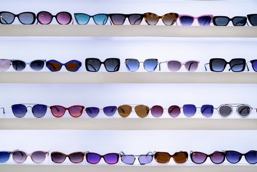 Sunglasses arranged on white shelves, showcasing diverse styles and vibrant lenses, organized selection, fashion accessories, retail environment, colorful shopping ambiance, front view. photo
