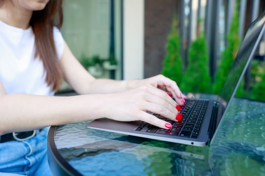 Close-up of woman hands typing on laptop outdoors. She has bright red nails, and the glass table photo