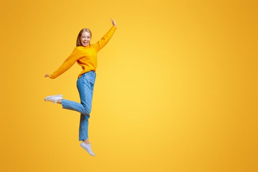 Be yourself. Pretty young girl jumping in air and laughing on orange background, free space photo