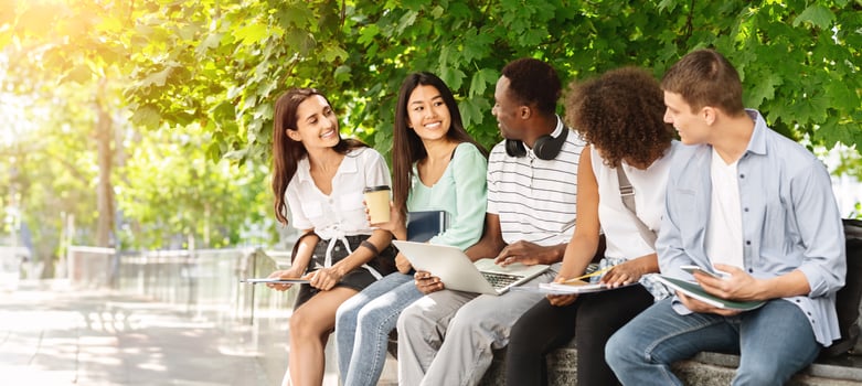 Cheerful college students having discussion outdoors while sitting on bench in university campus, preparing for exams or having break between classes photo