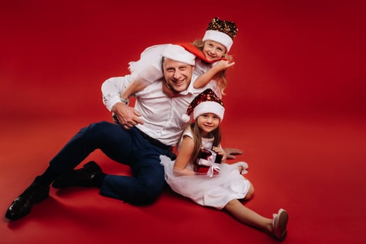 Portrait of a happy family in a Christmas hat on a red background. Dad and daughters at Christmas photo