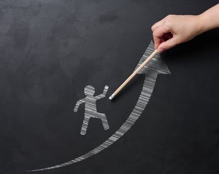 A hand draws a picture of a person walking on an upward arrow on a blackboard with chalk, symbolizing personal growth, success and progress. Concept of development and goal achievement photo