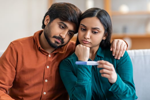 A loving Indian couple sits close together in their living room, both intently focused on a pregnancy test. The man has his arm around the woman, offering comfort and support as they await the results photo