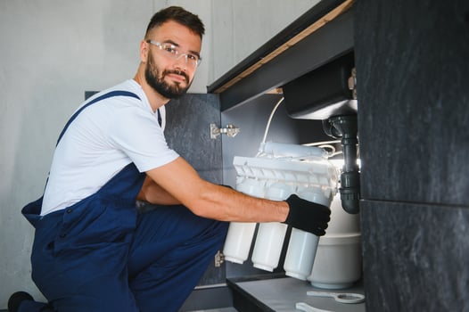 Plumber installs or change water filter. Replacement aqua filter. Repairman installing water filter cartridges in a kitchen. Installation of reverse osmosis water purification system photo
