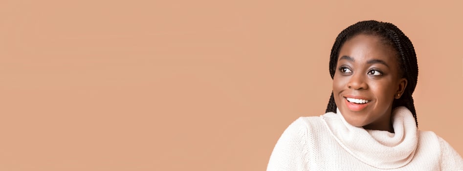 A young African American woman with braided hair smiles brightly, showcasing her joy and confidence. She is dressed in a cozy, light sweater, looking at copy space photo