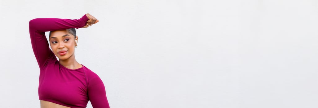 Athletic young black woman exercising on white background. Confident lady training over empty wall, wearing pink sportswear, holding bottle of water, looking at copy space. Hydration during workout photo