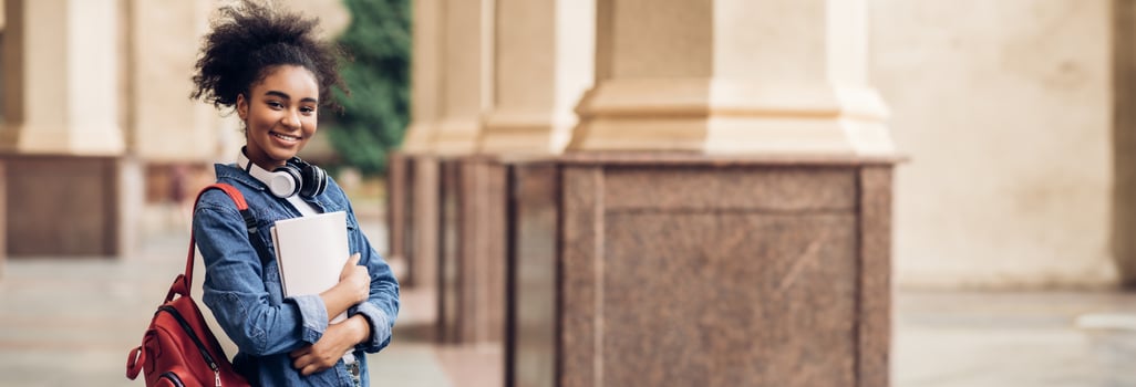 Cheerful Black Student Girl Hugging Books Posing With Backpack Near College Building Outdoor, Smiling To Camera. Modern Education, College Tuition And Grants, Studentship And Study Abroad, Copy Space photo