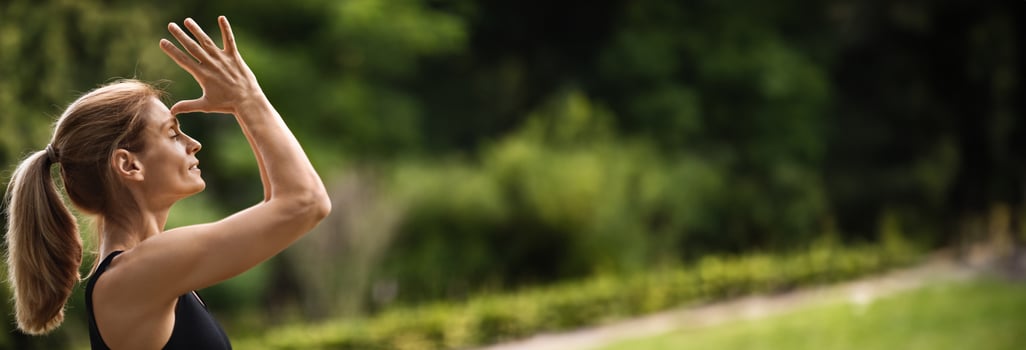 Side view of sporty young blonde woman practicing meditation at public park, holding hands next to face, eyes closed, enjoying yoga workout outdoors, closeup, panorama with copy space photo