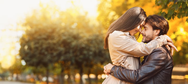 Loving young couple cuddling over golden forest background, touching each other with foreheads photo