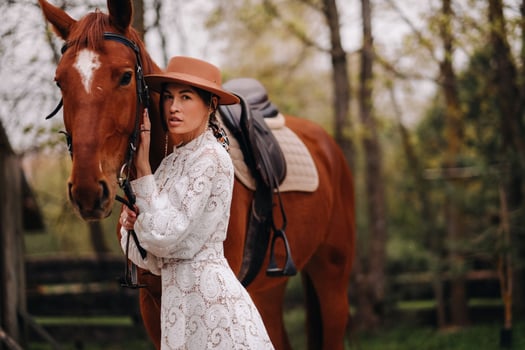 A girl in a white dress and a hat is standing next to a horse photo