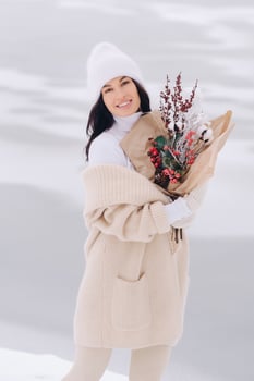 A girl in a beige cardigan and winter flowers walks in nature in the snowy season. Winter weather photo
