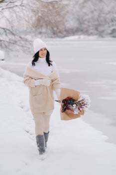 A girl in a beige cardigan and winter flowers walks in nature in the snowy season. Winter weather photo