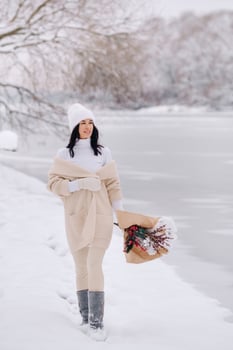 A girl in a beige cardigan and winter flowers walks in nature in the snowy season. Winter weather photo