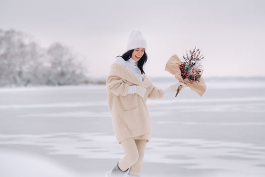 A girl in a beige cardigan and winter flowers walks in nature in the snowy season. Winter weather photo