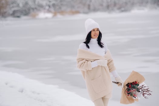 A girl in a beige cardigan and winter flowers walks in nature in the snowy season. Winter weather photo
