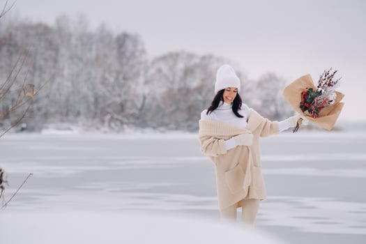 A girl in a beige cardigan and winter flowers walks in nature in the snowy season. Winter weather photo