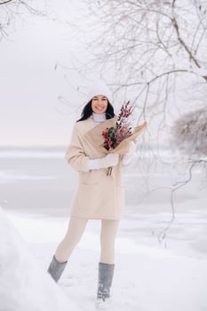 A girl in a beige cardigan and winter flowers walks in nature in the snowy season. Winter weather photo