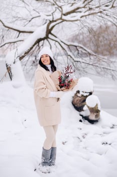 A girl in a beige cardigan and winter flowers walks in nature in the snowy season. Winter weather photo