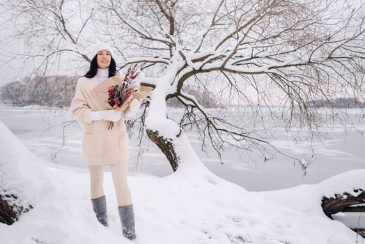 A girl in a beige cardigan and winter flowers walks in nature in the snowy season. Winter weather photo