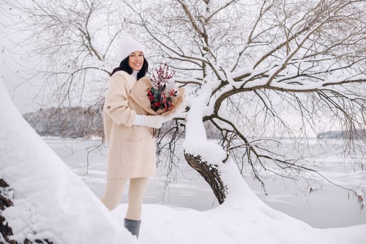 A girl in a beige cardigan and winter flowers walks in nature in the snowy season. Winter weather photo
