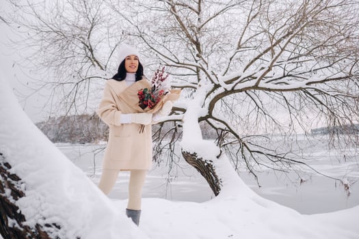 A girl in a beige cardigan and winter flowers walks in nature in the snowy season. Winter weather photo