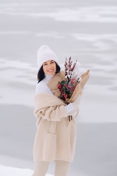 A girl in a beige cardigan and winter flowers walks in nature in the snowy season. Winter weather photo