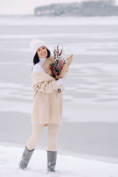 A girl in a beige cardigan and winter flowers walks in nature in the snowy season. Winter weather photo