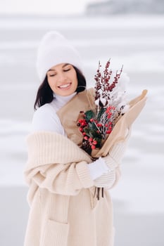 A girl in a beige cardigan and winter flowers walks in nature in the snowy season. Winter weather photo