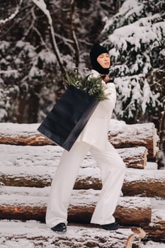 A girl in a white suit and balaclava with a package of Christmas trees in the winter forest on New Year's Eve.New Year's concept photo