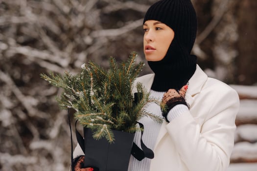 A girl in a white suit and balaclava with a package of Christmas trees in the winter forest on New Year's Eve.New Year's concept photo