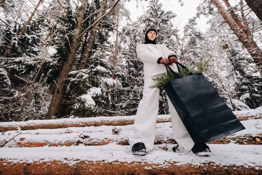 A girl in a white suit and balaclava with a package of Christmas trees in the winter forest on New Year's Eve.New Year's concept photo