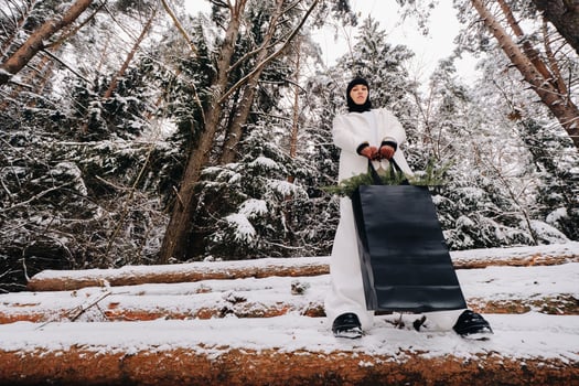 A girl in a white suit and balaclava with a package of Christmas trees in the winter forest on New Year's Eve.New Year's concept photo
