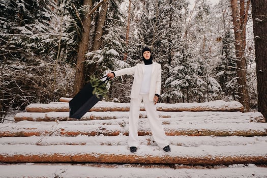 A girl in a white suit and balaclava with a package of Christmas trees in the winter forest on New Year's Eve.New Year's concept photo