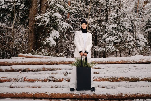 A girl in a white suit and balaclava with a package of Christmas trees in the winter forest on New Year's Eve.New Year's concept photo