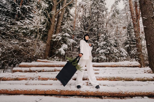 A girl in a white suit and balaclava with a package of Christmas trees in the winter forest on New Year's Eve.New Year's concept photo