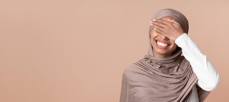 Facepalm. Cheerful Black Muslim Woman In Headscarf Covering Eyes With Hand And Laughing, Feeling Shy, Standing Over Yellow Background, Copy Space photo