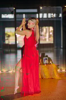 A girl in a red dress moves in a dance meditating indoors . Dynamic dance photo