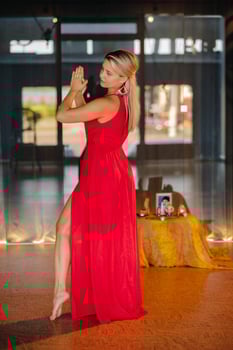 A girl in a red dress moves in a dance meditating indoors . Dynamic dance photo