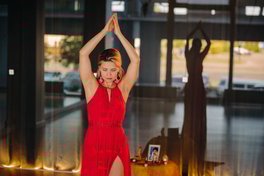A girl in a red dress moves in a dance meditating indoors . Dynamic dance photo