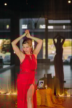A girl in a red dress moves in a dance meditating indoors . Dynamic dance photo
