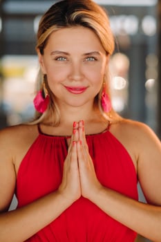 Portrait of a smiling girl in a red dress stands in the interior with her hands clasped in front of her photo