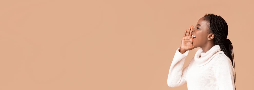 Black woman with braided hair actively shouts with enthusiasm, showcasing her expressive energy. She is dressed in a cozy white sweater, and her pose suggests a moment of engagement or communication photo