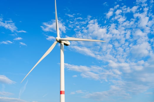A lone wind turbine stands tall against a blue sky with fluffy clouds. The turbines white blades spin slowly, capturing wind energy and converting it into clean electricity. photo