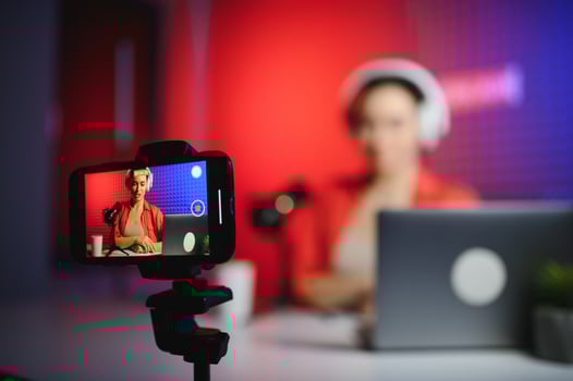 Positive trendy blogger woman speaking at smartphone webcam on tripod, recording post for vlog photo